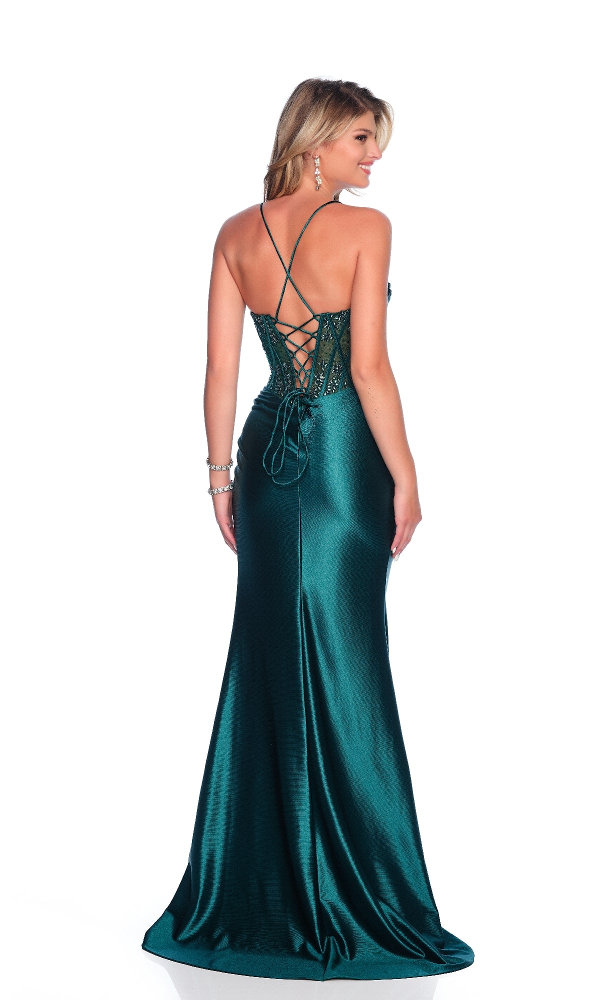 A woman stands facing away, wearing the Dave & Johnny 12203 Lace-Up Green Prom Dress featuring a long emerald skirt, sheer corset bodice, lace-up back, and thin straps.